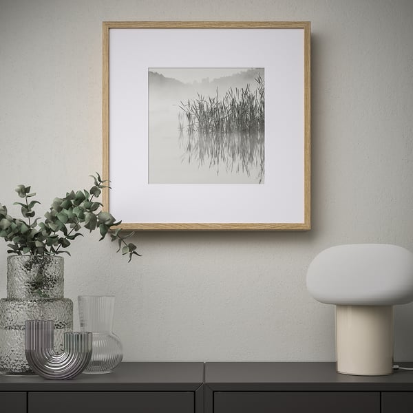 Framed landscape art on wall with vases and lamp.