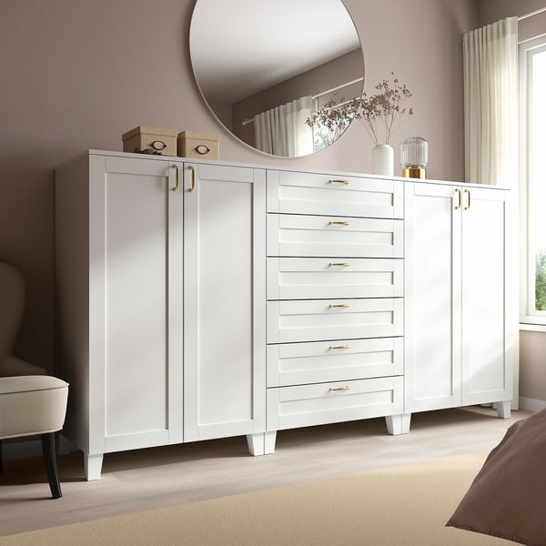 White storage set with drawers, tall cabinets, mirror, gold handles, near bed and chair