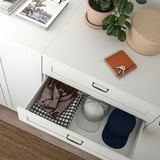 Open SANNIDAL drawer with folded clothes: checkered shirt, denim jacket, caps.