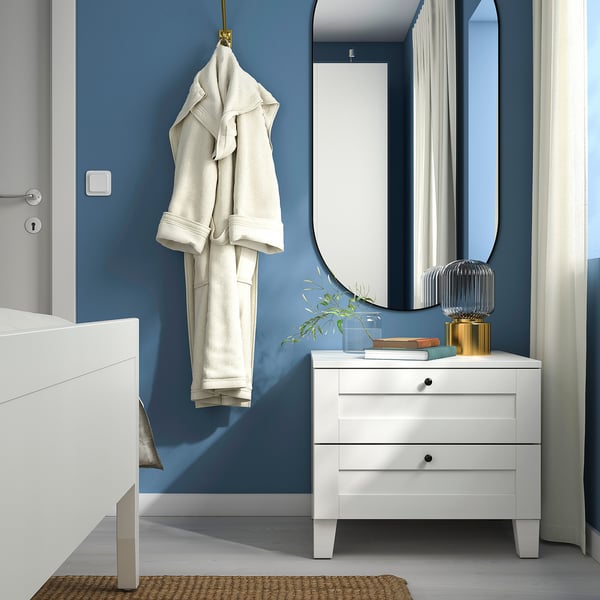 Modern bedroom with blue walls; white SANNIDAL bedside table, hanging robe, large mirror, and decorative pieces.