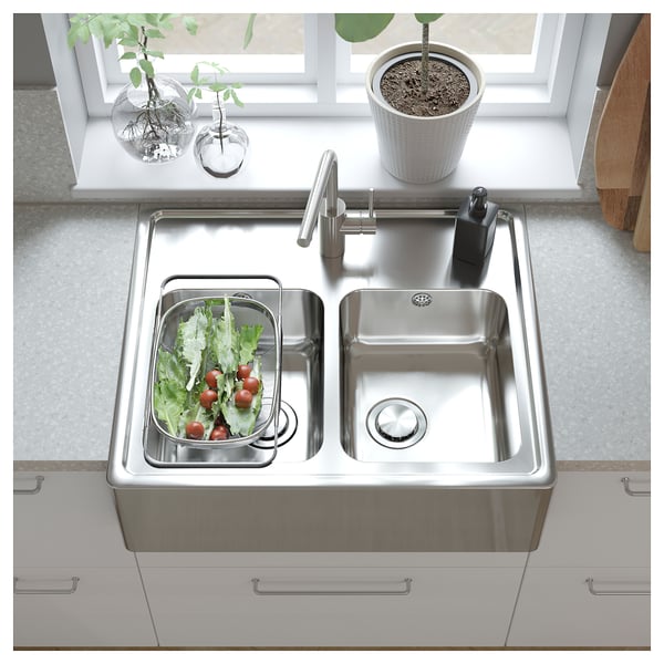 Modern kitchen with stainless steel double sink, fresh veggies in strainer, white countertop, and potted plant.