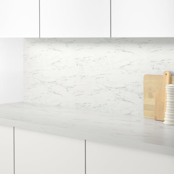 Modern kitchen counter with white marble-patterned backsplash, featuring light wood cutting boards and a white vase.