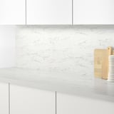 Modern kitchen counter with white marble-patterned backsplash, featuring light wood cutting boards and a white vase.