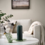Green powder-coated steel candle holder with chinese-inspired pattern on table, with white blanket, vase, and framed picture.