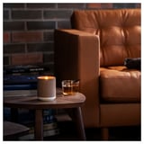 Brown leather chair beside wooden table with lit beige candle and whiskey glass. Cozy indoor setting.