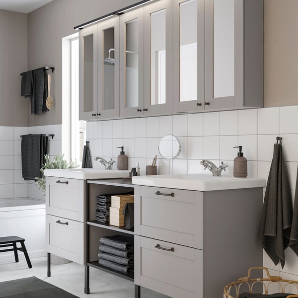Modern grey bathroom with dual sink, mirror, glass storage, towels, and decor.
