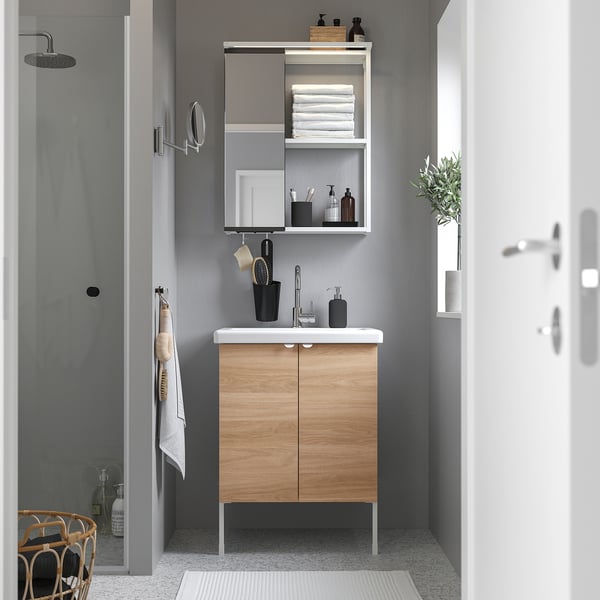 Small modern wooden vanity with sink and mirror, placed between shower and door, with black accents and white countertop.