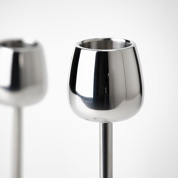 Two sleek, shiny stainless steel candlesticks with polished surfaces and smooth, curved lines. One in foreground, another blurred in background.