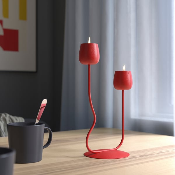 Red candlestick with two lit candles, sitting on a wooden table next to a mug with a spoon.