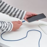 Person charging phone with SITTBRUNN usb-c cable, shown holding phone and plug.