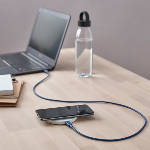 A workspace with a charging smartphone, laptop, and water bottle. The phone is connected via a blue usb-c cable.