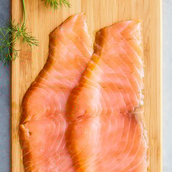 Pink salmon fillets on wooden board with green herbs.