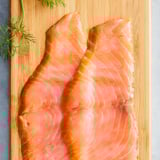 Pink salmon fillets on wooden board with green herbs.