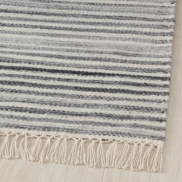 Striped woven wool rug, handmade with fringe edges, on light wooden floor.