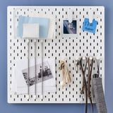 White SKÅDIS pegboard with accessories: mesh basket, notes, photos, keys, purse, and umbrella hooks. Ideal for organizing and displaying items.