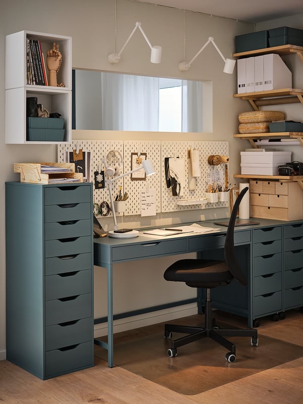Modern home office featuring SKÅDIS blue-green pegboard setup, black chair, and gray desk with organized storage shelves and a whiteboard.
