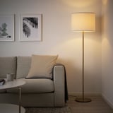 Modern living room with SKAFTET floor lamp, white shade. Gray sofa, pillows, near wall decorations.