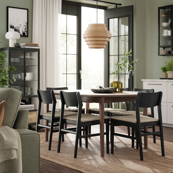Modern dining area with dark wood table, chairs, green accent wall, large window, and pendant light.