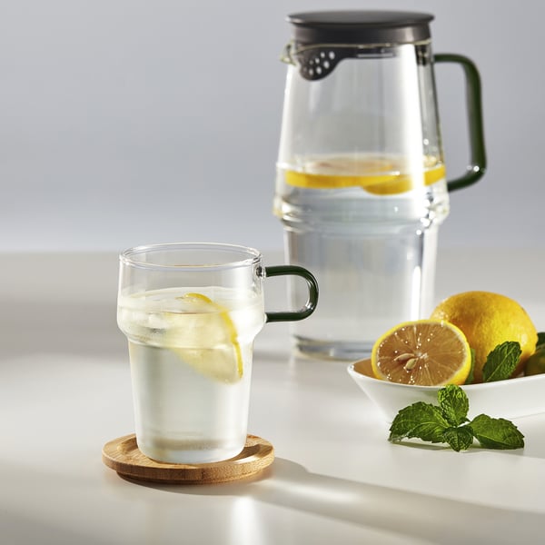 Glass mug with handle and pitcher, lemons, ice, mint; refreshing drink setup.