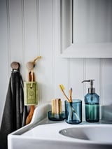 Modern bathroom with white sink, teal soap dispenser & toothbrush holder, gray towel on hooks.
