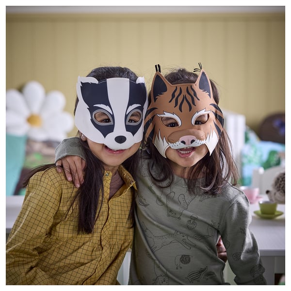 Two kids in badger & lynx masks smile in cozy room.