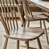 SKOGSTA chairs: light brown, wooden, arched back, spindle design. Slim, fits well in spaces.
