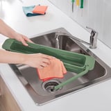 Green skola sink organizer with cloth, dishcloth, and metallic sink drain.