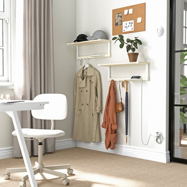 A well-organized corner with a SKOMAKARE unit in white holding coat, umbrella, plant, and phone. A white office chair nearby.