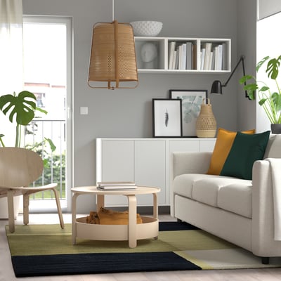 Living room with SKRIFTSPRÅK rug, grey sofa, side table, plants, and shelves with books.
