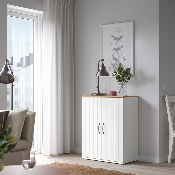 A cozy living room featuring a white SKRUVBY cabinet with double doors, oak top, and black decor. Balanced with a window and chair.