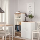 SKRUVBY storage unit in living space. White, adjustable shelves, warm wooden top, between chairs.