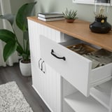 White cabinet with open drawer revealing plates and cloths, wooden top with books and plant.