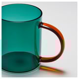 Turquoise glass mug with orange handle, reflecting light, showcasing smooth texture and ergonomic design.