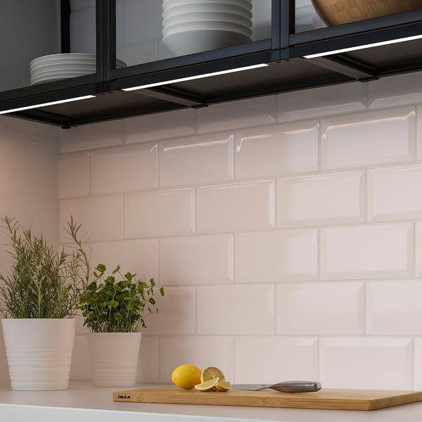 Kitchen counter with herbs, lemon, knife, and lighting under shelves.