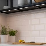 Kitchen counter with herbs, lemon, knife, and lighting under shelves.