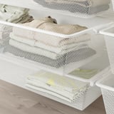 White mesh storage drawers organized with folded clothes on a wooden floor. Part of the boaxel wall-mounted storage system, great for saving space.