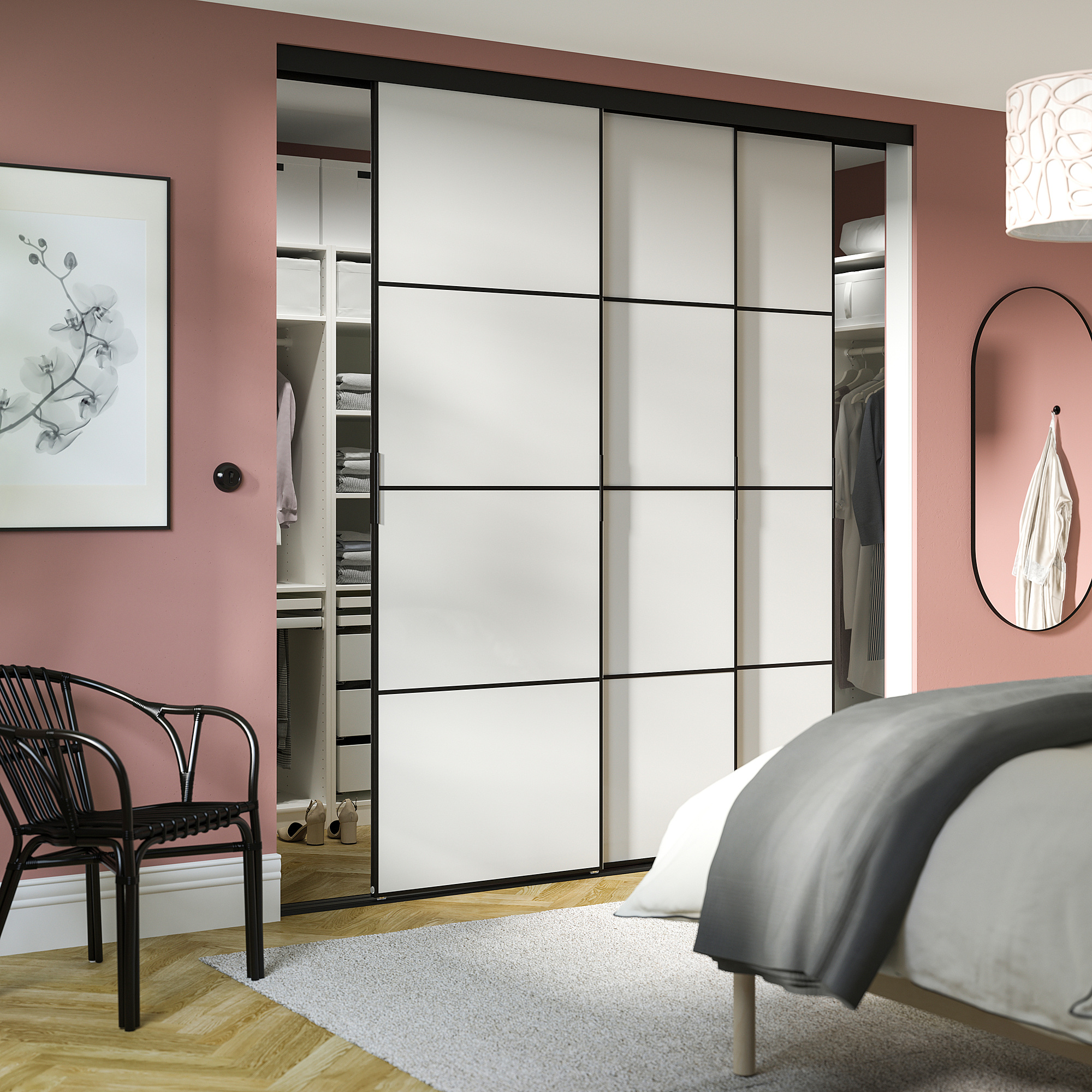Modern bedroom with large white closet, black chair, rounded mirror on pink wall, and grey bedding.