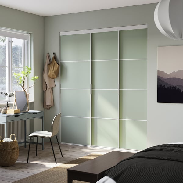 Modern bedroom with light green frosted glass closet doors, wooden floor, and minimalist decor.
