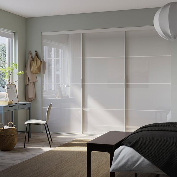 SKYTTA door unit in a bedroom with white sliding panels, modern design. Its large, nearly covering the wall behind the bed, which is small.