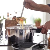 Cook lifts noodles from stainless saucepan, SLÄTROCKAs detachable handle shown.