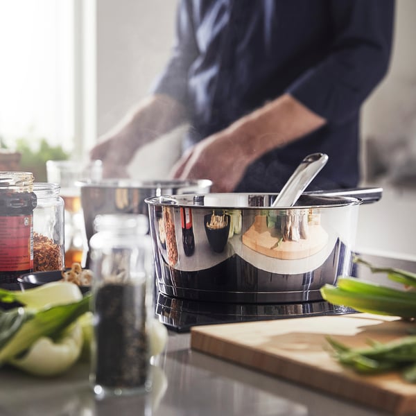 Person cooking with stainless steel saucepan on kitchen counter.
