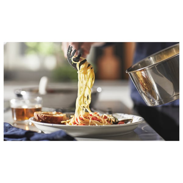 Chef serving spaghetti with colorful veggies onto a plate. Saucepan with removable handle is seen on the side.