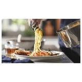 Chef serving spaghetti with colorful veggies onto a plate. Saucepan with removable handle is seen on the side.