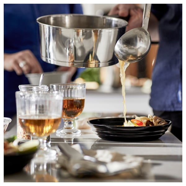 Pouring liquid from ladle to bowl on counter with glasses.