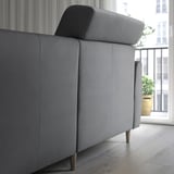 Modern gray sofa with extendable back cushions for head support, positioned near a large window with balcony view.