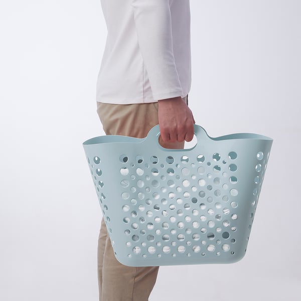 Person holding light blue perforated laundry basket, designed for carrying and storing clothes.