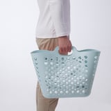 Person holding light blue perforated laundry basket, designed for carrying and storing clothes.