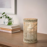 Beige woven lantern on wooden table, candlelit, smaller than books and vase.