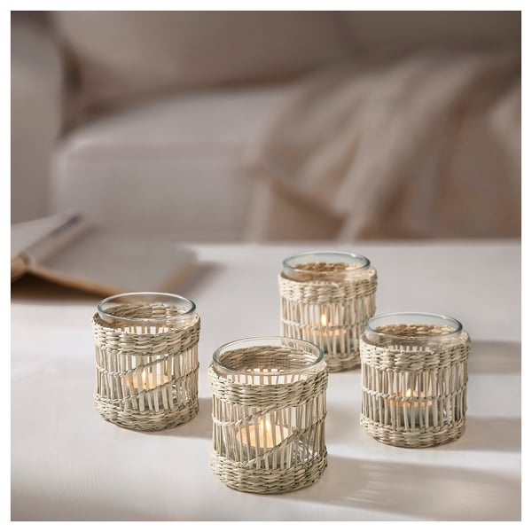 Four handwoven sedge tealight holders in natural beige color arranged on a white surface, each with a lit candle, showcasing rustic, circular design.