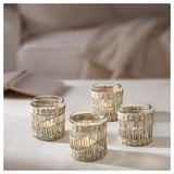 Four handwoven sedge tealight holders in natural beige color arranged on a white surface, each with a lit candle, showcasing rustic, circular design.